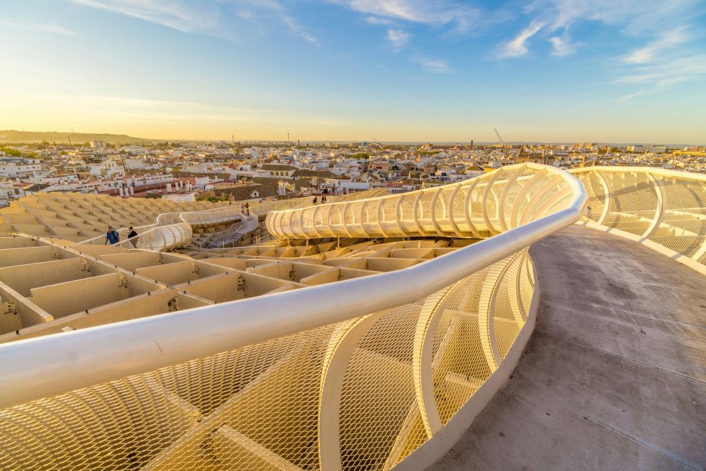 석양이 질 무렵 도시 경관이 내려다보이는 그물 난간이 있는 곡선형 통로. 경로에 표시되는 사람은 거의 없습니다.