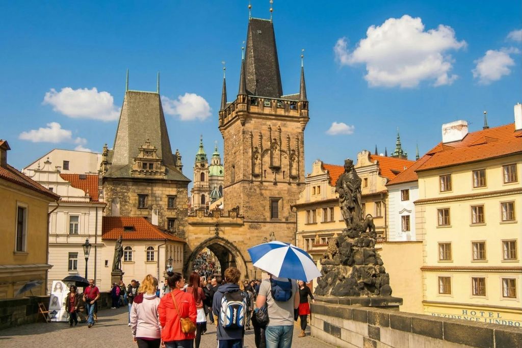 역사적인 건축물, 높은 고딕 타워, 맑고 푸른 하늘 아래를 걷는 관광객이 있는 번화한 유럽 거리.