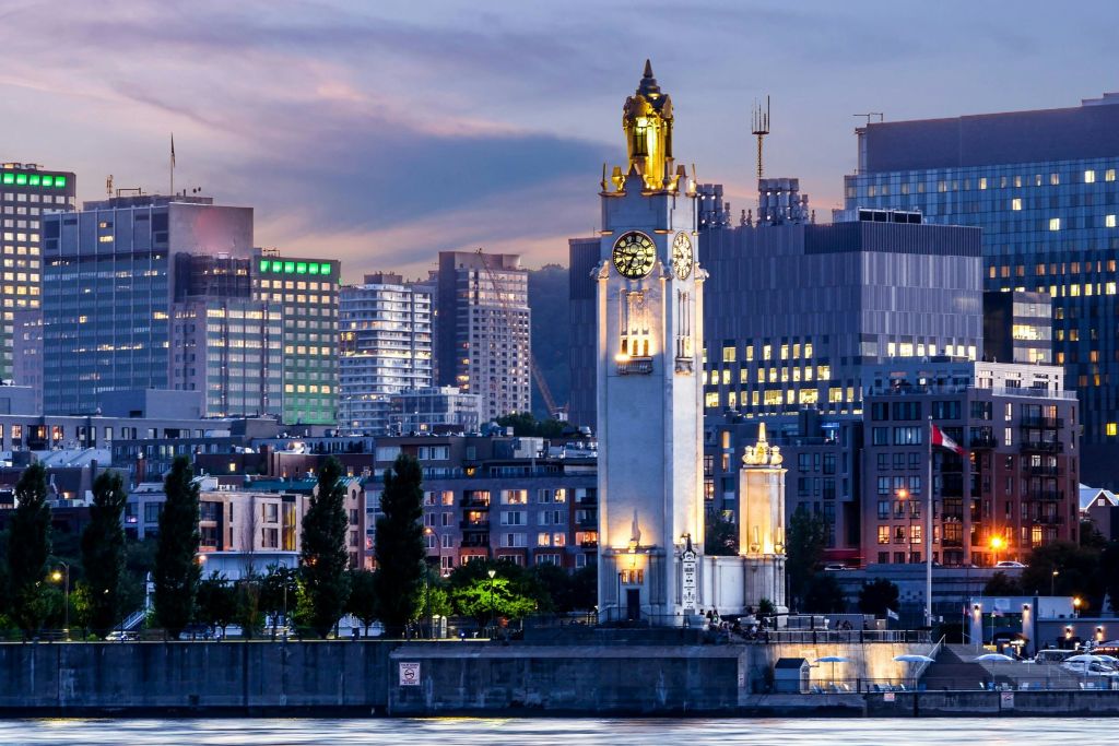 해질 무렵 해안가를 따라 현대적인 건물과 나무로 둘러싸인 시계탑입니다.