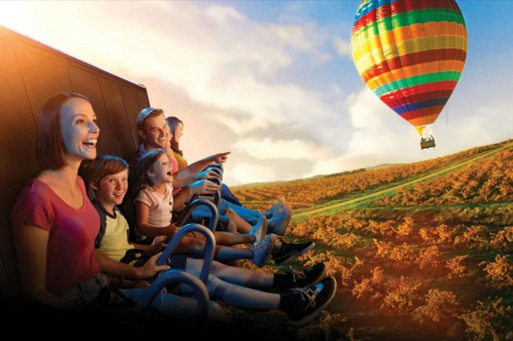 앉아서 안전하게 놀이기구를 타고 있는 한 무리의 사람들이 미소를 지으며 햇살이 내리쬐는 풍경의 경치를 바라보고 있습니다.