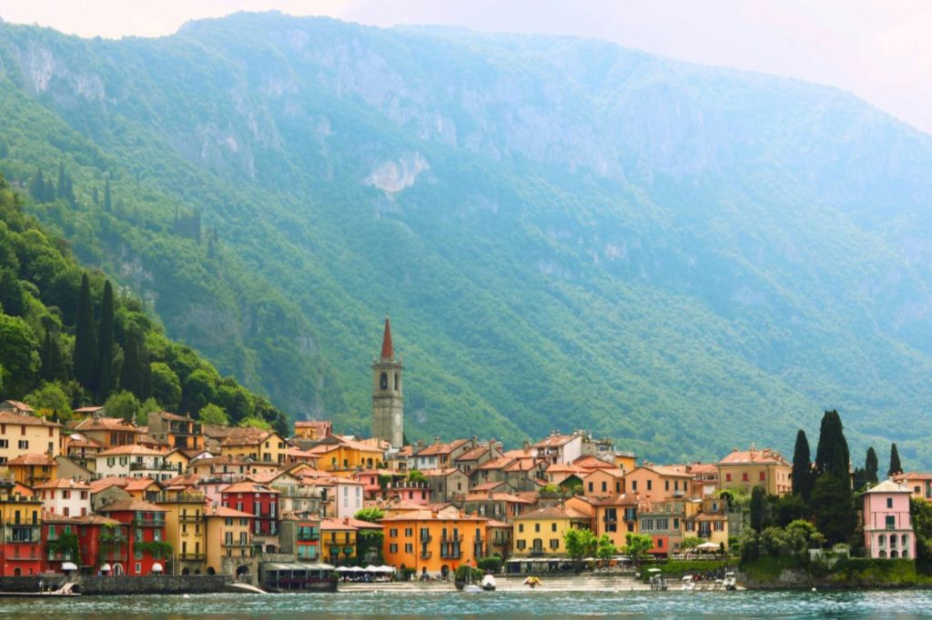 화려한 건물, 종탑, 울창하고 푸른 산을 배경으로 한 독특한 호숫가 마을입니다.