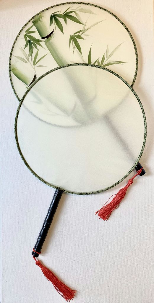 밝은 색상의 원단, 녹색 가장자리 및 검은색 손잡이가 있는 두 개의 전통적인 둥근 손 선풍기. 하나는 빨간색 태슬이 달려 있습니다.