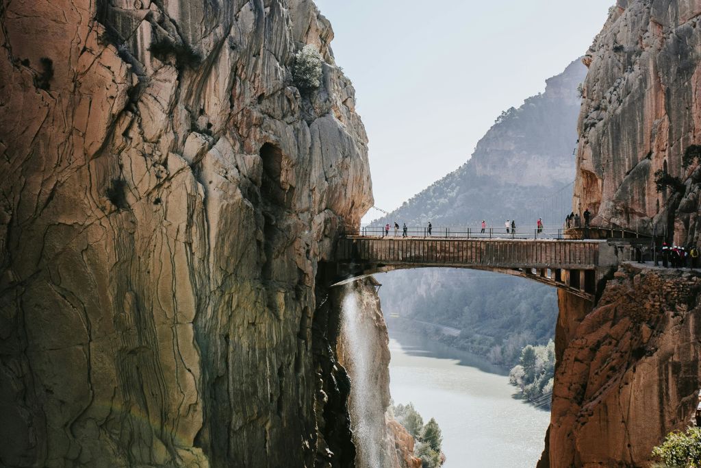 보행자 다리는 강을 가로지르는 두 개의 절벽 사이에 있으며, 그 위를 걷는 사람들이 있고 그 아래로 폭포가 보입니다.