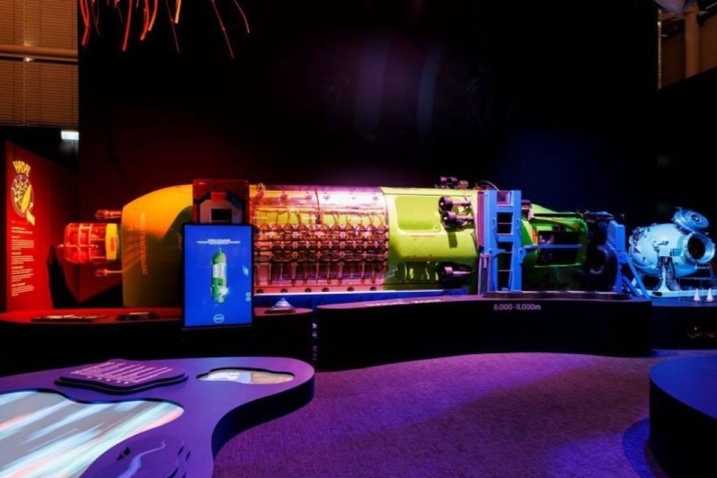 어두운 전시회에 전시된 녹색 미래형 잠수정 모델로, 정보 화면과 주변 장식이 있습니다.