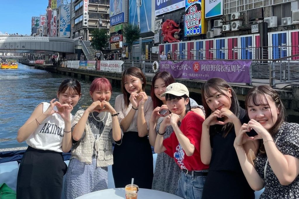 운하 근처 야외에서 포즈를 취하는 7명의 여성 그룹이 화려한 도시 건물을 배경으로 손짓을 하고 있습니다.