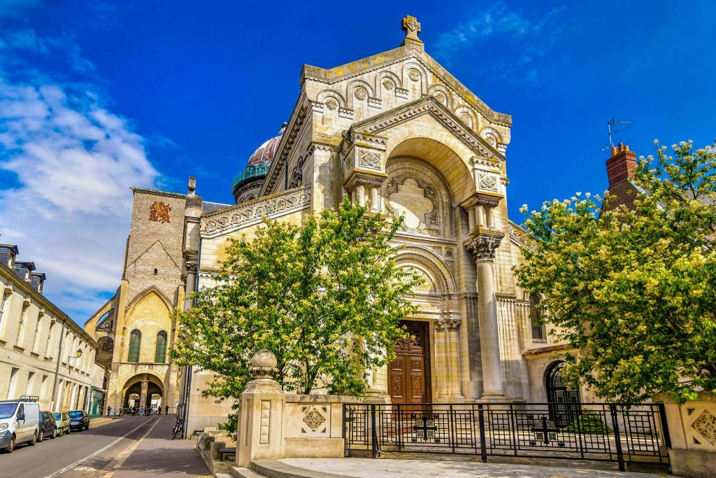 화려한 건축물과 나무가 앞에 있고, 맑고 푸른 하늘을 배경으로 한 유서 깊은 교회입니다.