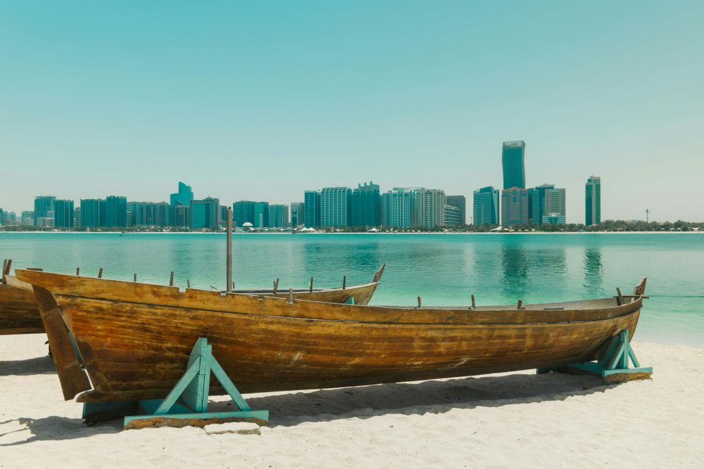 맑은 하늘 아래 도시의 스카이라인과 물을 배경으로 모래 해변에서 즐기는 나무 보트.