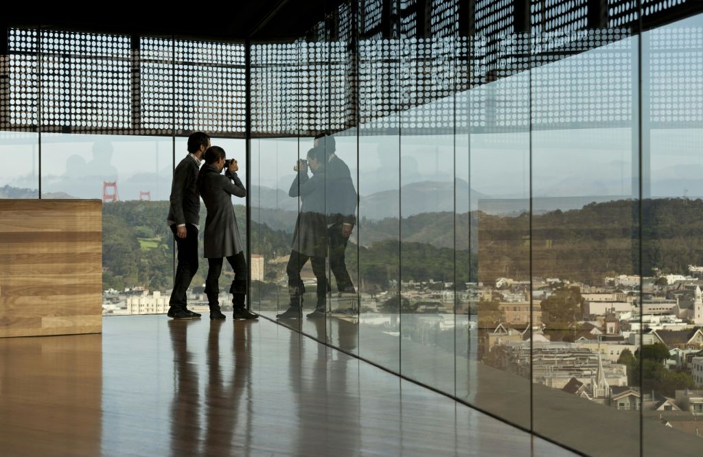 비즈니스 복장을 한 두 사람이 유리창에 도시와 풍경이 비친 천장부터 바닥까지 내려다보이는 창문을 통해 밖을 내다보고 있습니다.