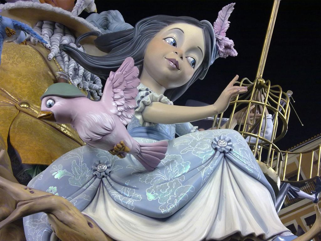 팔에 새를 달고 머리에 새장을 든 소녀의 동상입니다. 소녀는 꽃무늬 드레스를 입고 미소를 짓고 있습니다.