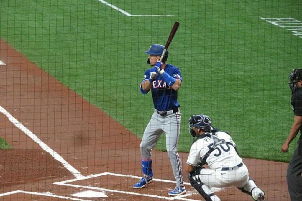 파란색 유니폼을 입은 야구 선수가 타석에 있고 흰색 유니폼을 입은 포수가 뒤에 웅크리고 있습니다.