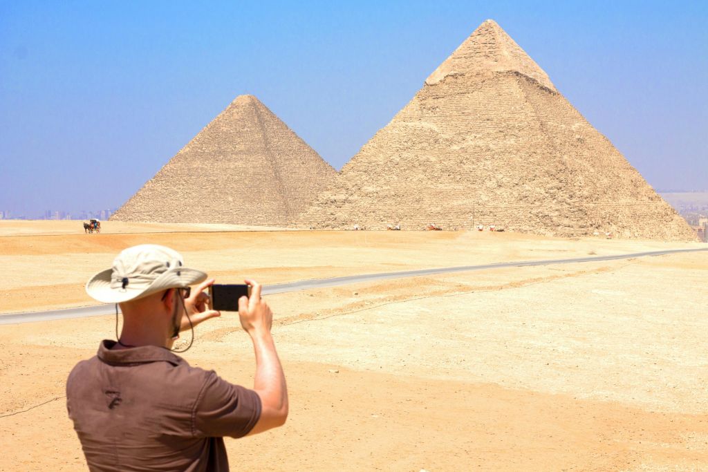 모자를 쓴 사람이 맑고 푸른 하늘을 배경으로 기자 피라미드 사진을 찍고 있습니다.