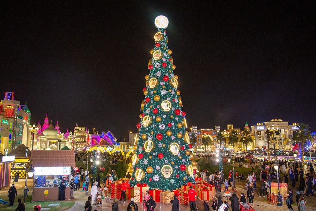 밤에는 활기찬 공공 광장에 장식품과 조명이 있는 크고 장식된 크리스마스 트리. 사람들이 모여들고 일부는 축제 복장을 하고 있습니다.