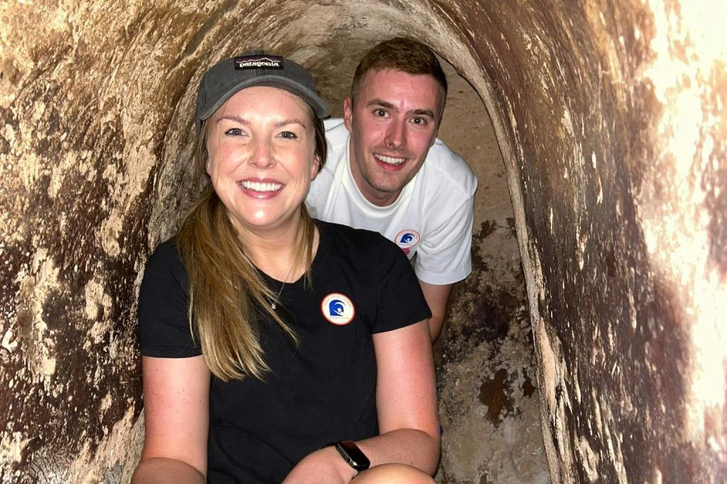 좁고 바위 같은 터널 안에서 웃고 있는 두 사람. 하나는 캡과 검은색 셔츠를, 다른 하나는 흰색 셔츠를 착용합니다.