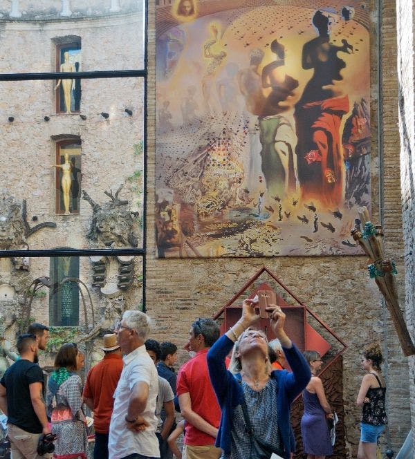 초현실주의 예술품이 전시된 건물 앞에 수많은 사람들이 서 있고, 한 사람이 스마트폰으로 사진을 찍고 있습니다.