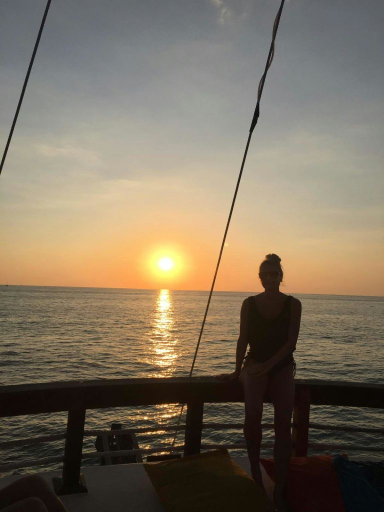 고요한 바다에 비친 태양과 함께 노을이 질 무렵 보트에 서 있는 사람. 부드러운 그라데이션으로 하늘이 맑습니다.