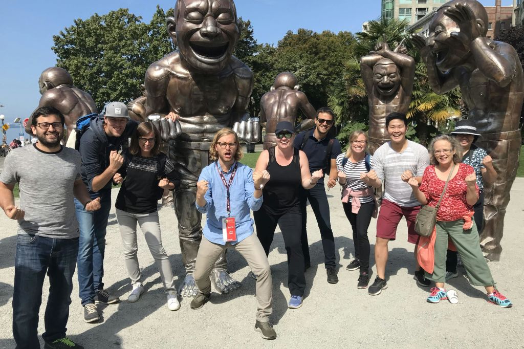 화창한 날 공원의 커다란 동상 앞에서 열정적인 포즈를 취하고 있는 한 무리의 사람들.