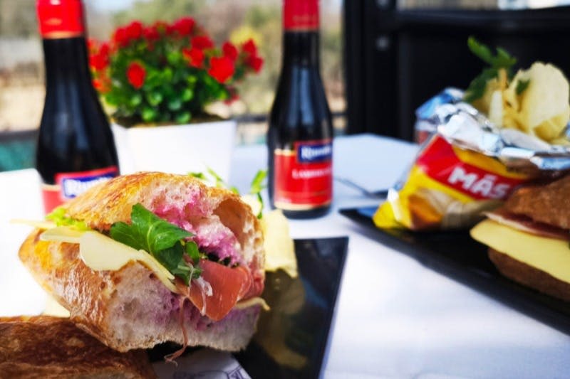 고기, 치즈, 채소가 들어간 샌드위치와 함께 과자 봉지, 와인 한 병, 화분을 배경으로 클로즈업한 사진입니다.