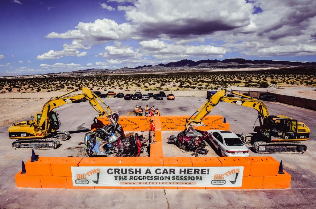 주황색 장벽 코스에서 자동차를 분쇄하는 두 대의 굴삭기. 사람들은 부분적으로 흐린 하늘 아래에서 배경을 보고 있습니다.