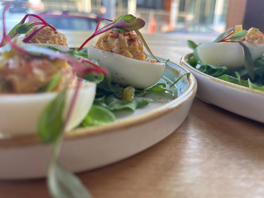 채소와 파프리카로 장식된 악마의 알 클로즈업이 나무 테이블 배경이 있는 흰색 접시에 담겨 제공됩니다.