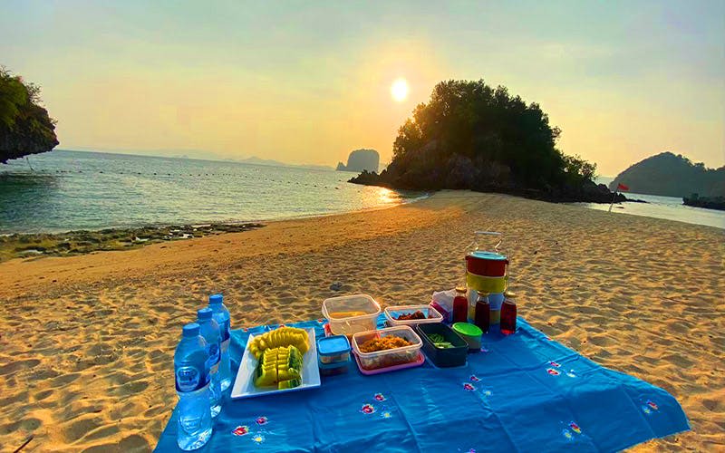해 질 녘 모래사장의 푸른 천에 물과 작은 섬을 배경으로 다양한 음식과 음료를 즐길 수 있습니다.