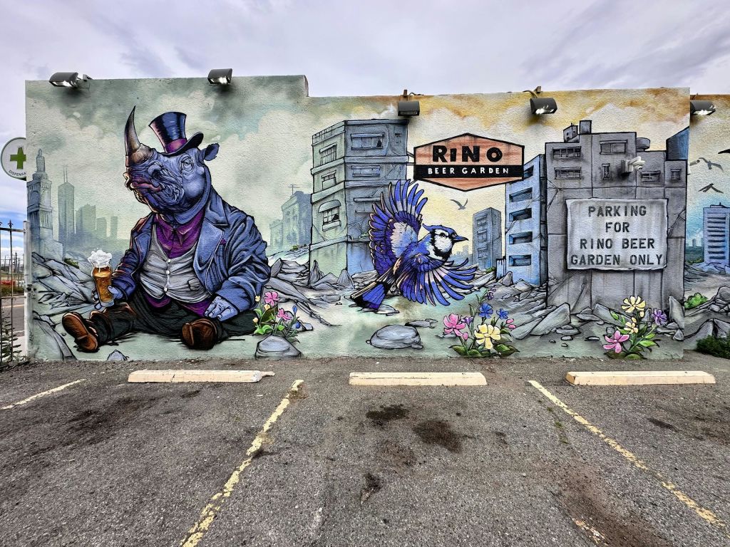 양복을 입은 코뿔소와 화려한 꽃 근처를 날아다니는 새가 건물을 배경으로 그려진 벽화.