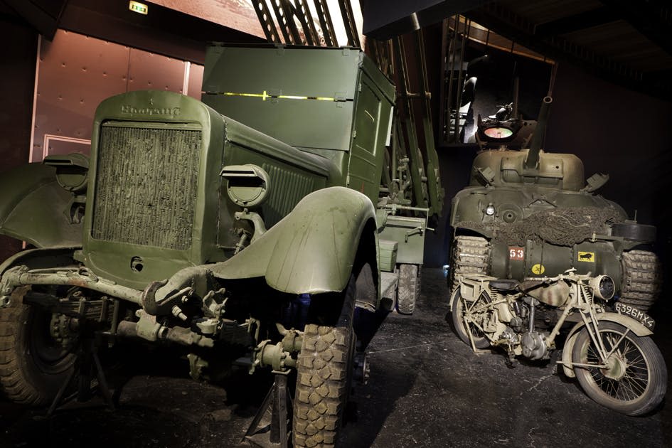 조명이 희미한 박물관 전시관에서 녹색 위장 페인트를 칠한 두 대의 빈티지 군용 차량. 차량 그릴의 텍스트에는 "Studebaker" 가 표시됩니다.