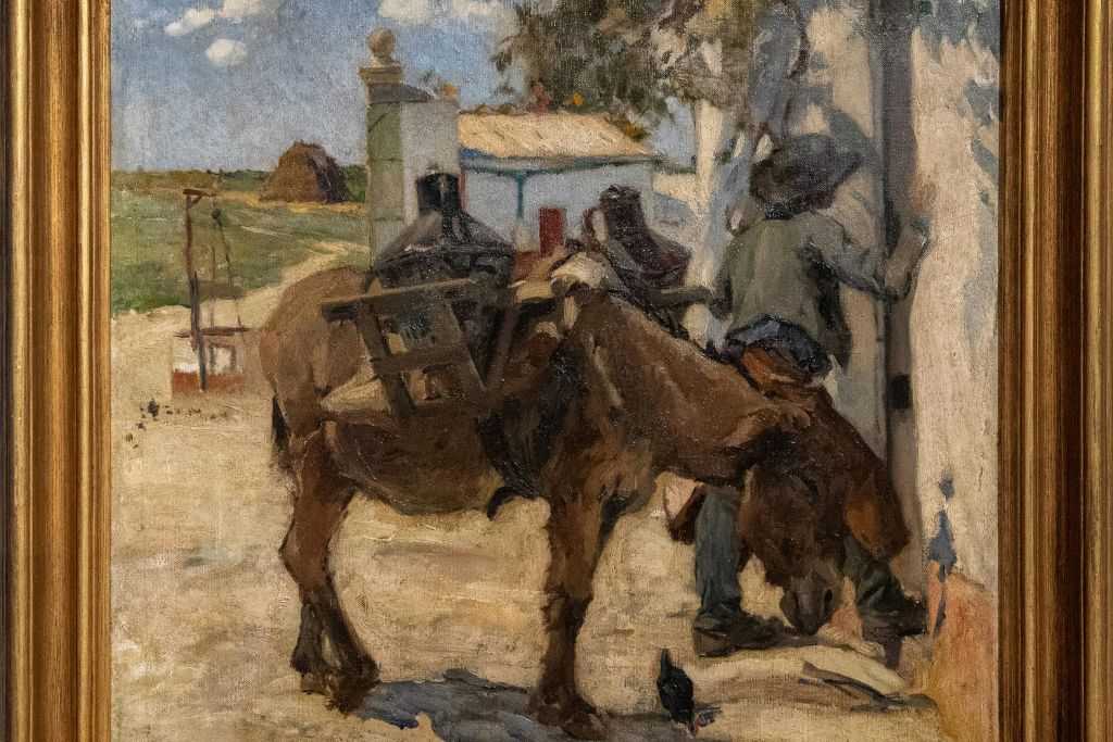 집과 건초더미를 배경으로 한 시골 풍경을 배경으로 당나귀가 안장가방을 메고 있는 남자의 그림.