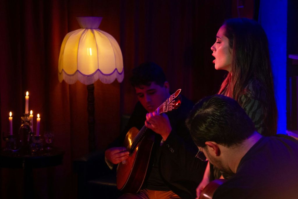 두 남자가 따뜻하고 푸른 무대 조명 아래에서 기타를 치는 동안 한 여성이 열정적으로 노래합니다.