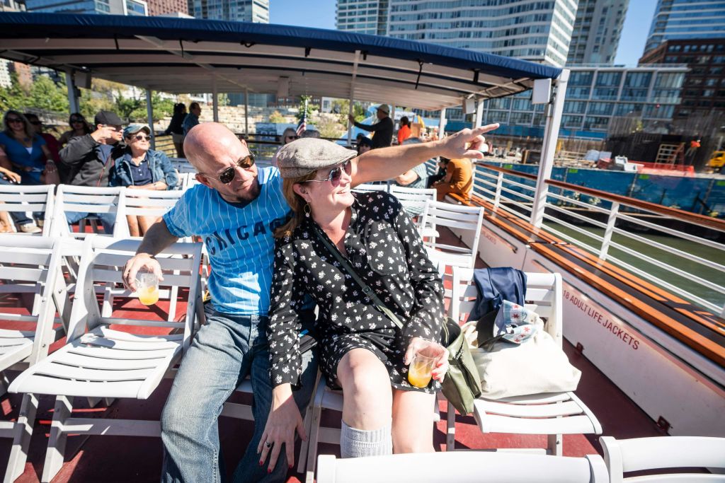 남자와 여자가 흰 좌석이 있는 보트에 앉아 있습니다. 남자는 음료를 들고 가리키고, 여자는 미소를 지으며 음료를 들고 있습니다.