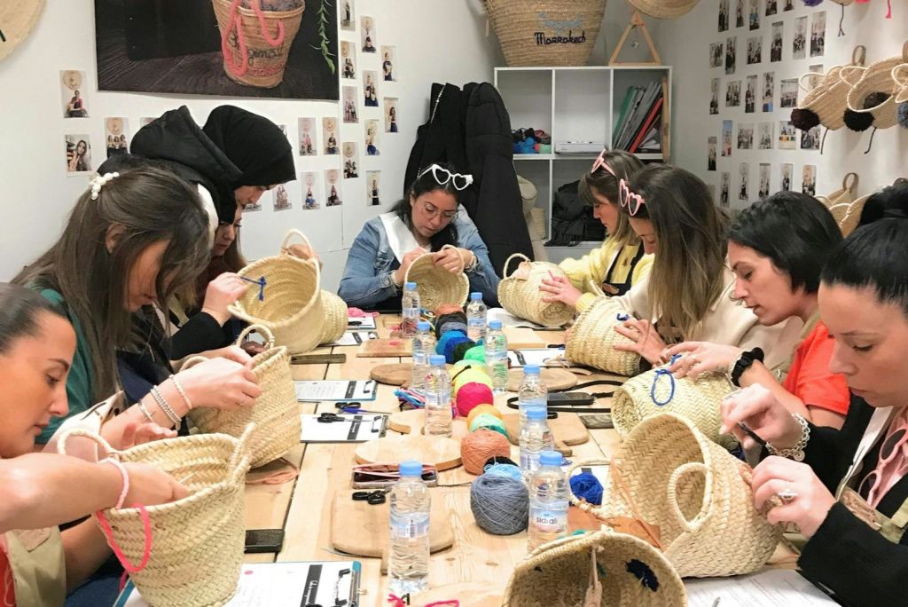 공예 워크숍에 참여한 한 무리의 여성들이 테이블 위에 화려한 원사와 도구로 짚 바구니를 장식하고 있습니다.