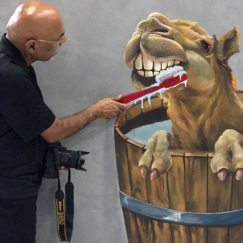 카메라를 든 남성이 벽화 속 통에 그려진 낙타의 이빨을 닦고 있습니다.