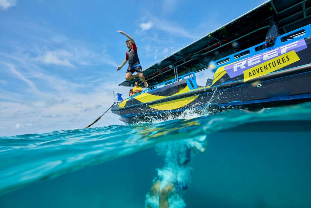 형형색색의 그래픽으로 보트에서 뛰어내려 맑고 푸른 물에 빠지는 사람, 아래에서 물속을 헤엄치는 또 다른 사람.