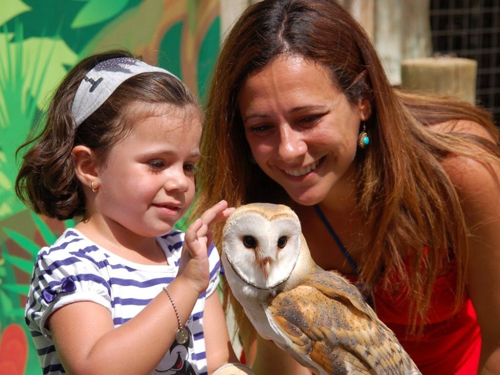 한 여성과 어린 소녀가 잎이 무성한 배경으로 헛간 올빼미를 부드럽게 만지며 웃고 있습니다.