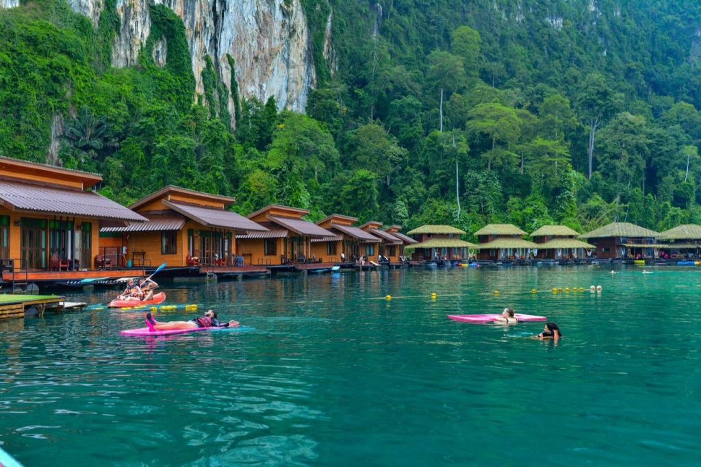 울창한 녹색 절벽으로 둘러싸인 떠다니는 나무 오두막 근처의 청록색 호수에서 패들보드에서 휴식을 취해보세요.