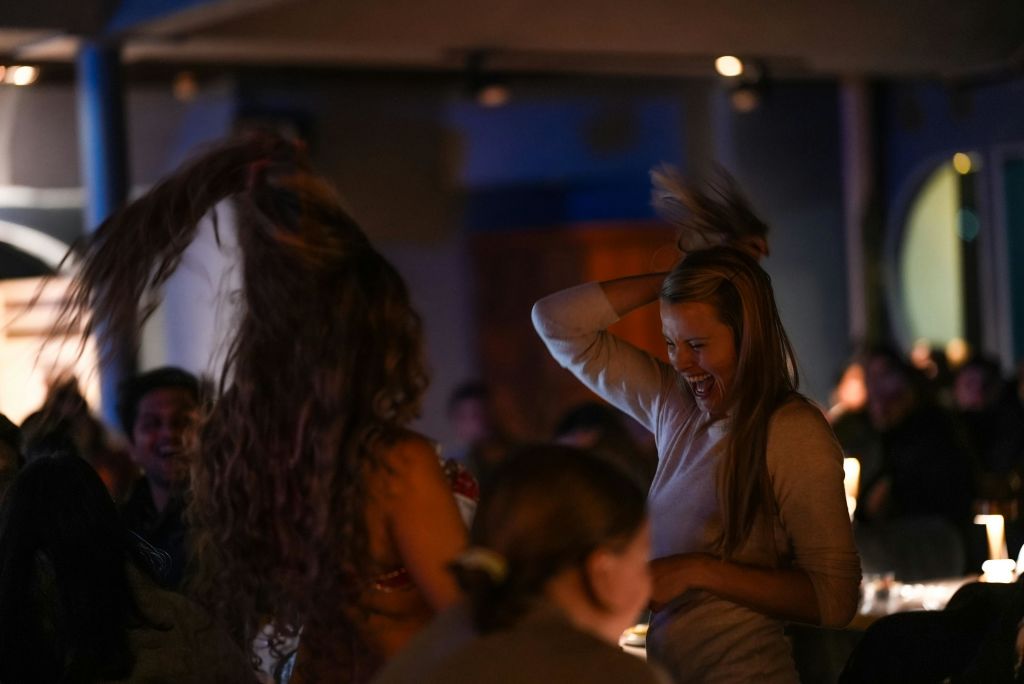 긴 머리를 한 여성이 어두운 조명으로 둘러싸인 실내에서 미소를 짓고 춤을 추고 있습니다.