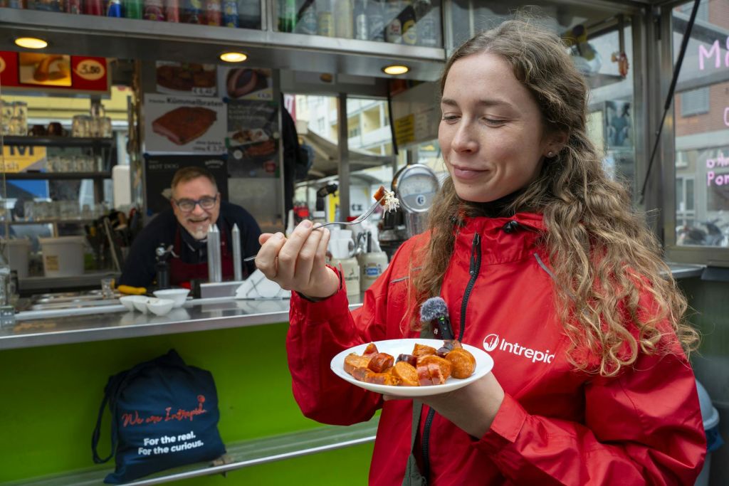 빨간 재킷을 입은 여성이 음식 가판대 앞에서 음식을 즐기고 있으며, 남성이 웃고 있습니다.