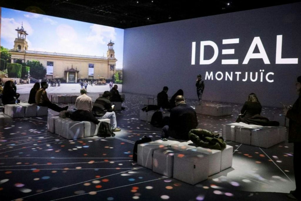 어두운 방에서 쿠션이 있는 벤치에 앉은 사람들은 커다란 화면에 비주얼을 표시하고 "IDEA MONTJ" 라고 문자를 보냅니다.