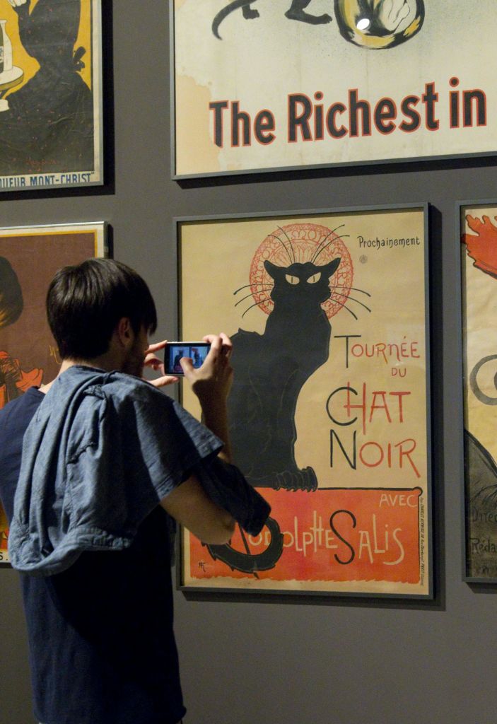 한 사람이 아트 갤러리에서 프랑스어 텍스트가 담긴 검은 고양이의 액자 포스터를 촬영하고 있습니다.