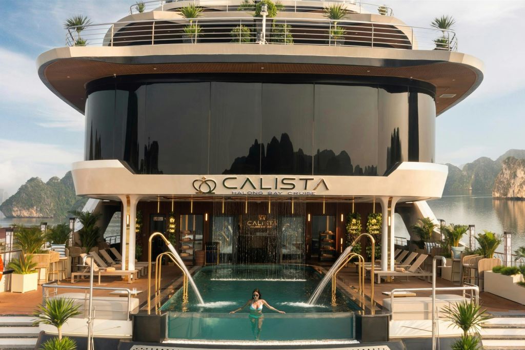 수영장과 계단식 폭포가 있는 고급 요트. 라운지 의자와 녹지가 배경을 장식하는 동안 한 여성이 수영을 하고 있습니다. "CALISTA" 표지판이 보입니다.