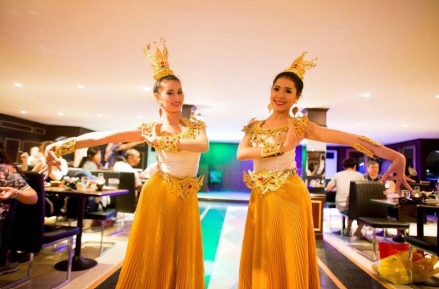 전통 의상을 입은 두 명의 여성이 레스토랑에서 춤을 추며 후원자들이 식사를 하고 있습니다.