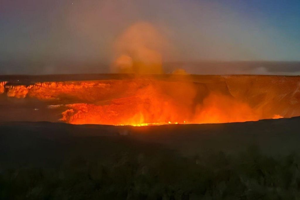 어두운 지형을 둘러싸고 있는 황혼의 하늘 아래에서 연기를 내뿜는 빛나는 용암 분화구.