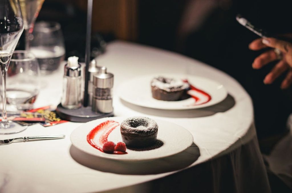 흰색 식탁보에 빨간색 소스와 라즈베리로 장식된 초콜릿 디저트가 담긴 접시 2개.