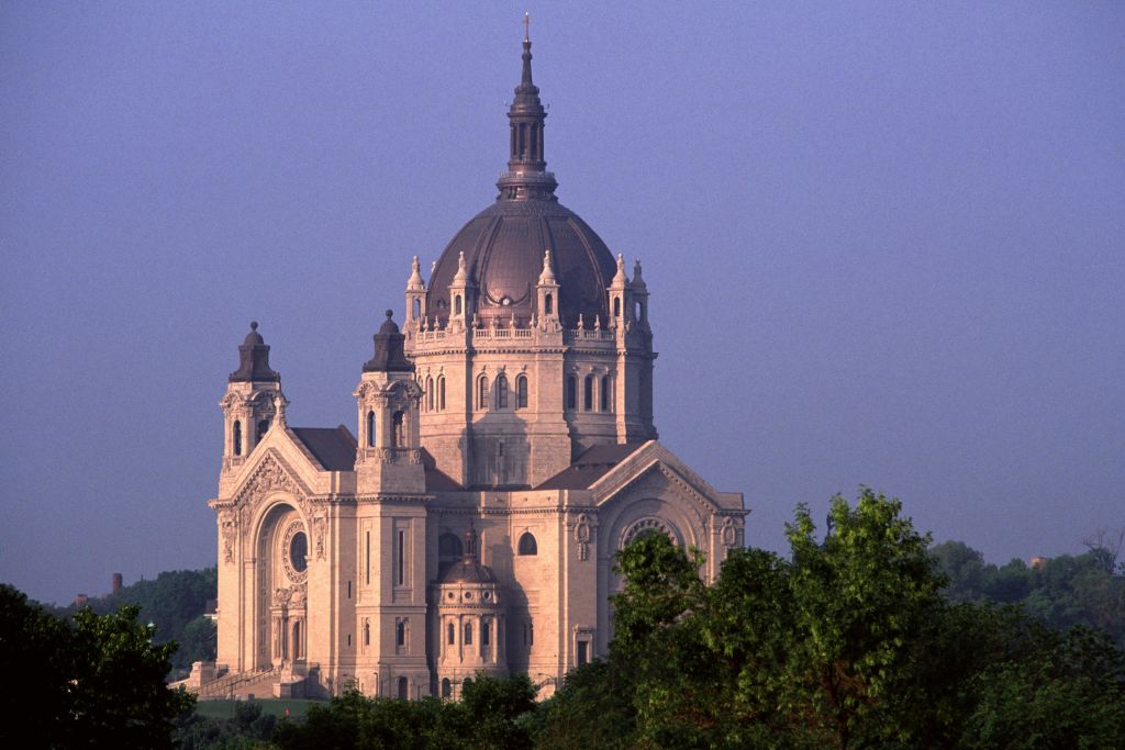 멀리 보이는 커다란 돔과 첨탑이 있는 대성당으로, 맑은 하늘 아래 나무로 둘러싸여 있습니다.