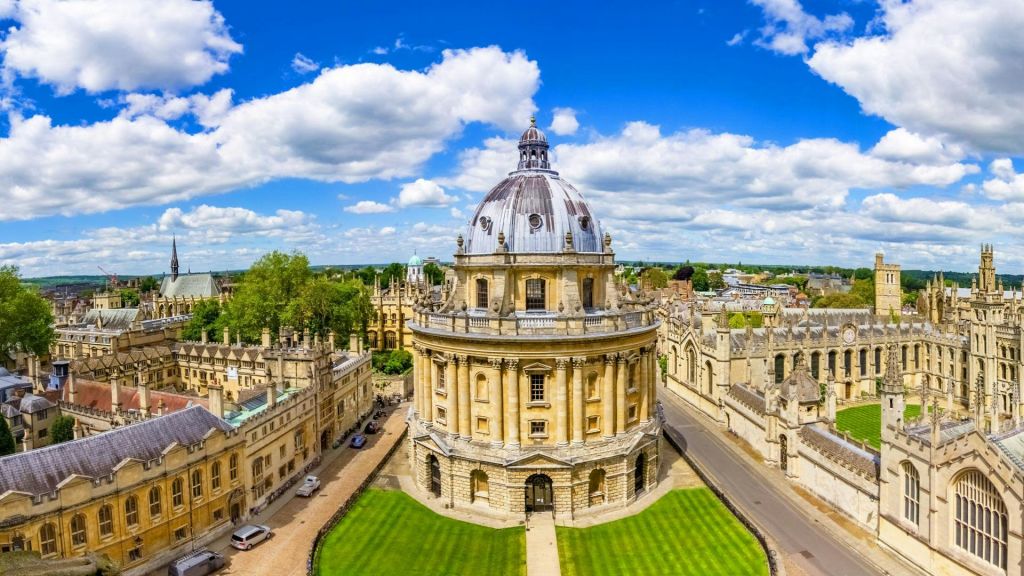 푸른 잔디밭과 돌길로 둘러싸인 유서 깊은 돔형 건물의 공중 전망을 감상할 수 있으며, 구름이 흩날리는 푸른 하늘 아래 자리잡고 있습니다.