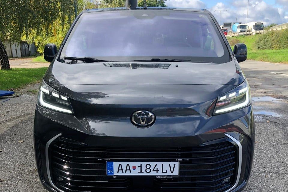 "AA 184 LV" 라고 적힌 유럽 번호판이 있는 검은색 도요타 차량이 나무와 푸른 하늘을 배경으로 야외에 주차되어 있습니다.