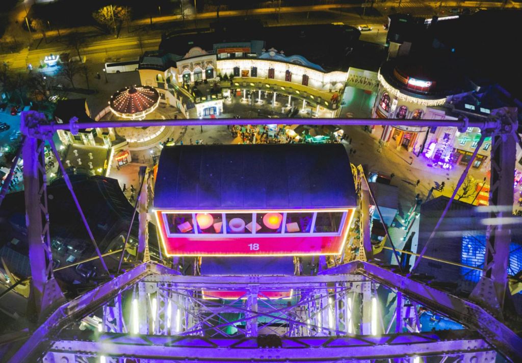 대관람차에서 빛나는 놀이공원 건물과 밤에 사람들이 있는 곤돌라를 내려다보는 풍경.