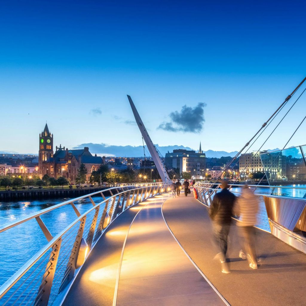 황혼이 질 무렵, 도시 풍경과 교회를 배경으로 조명이 켜진 현대적인 다리를 걸어보세요.