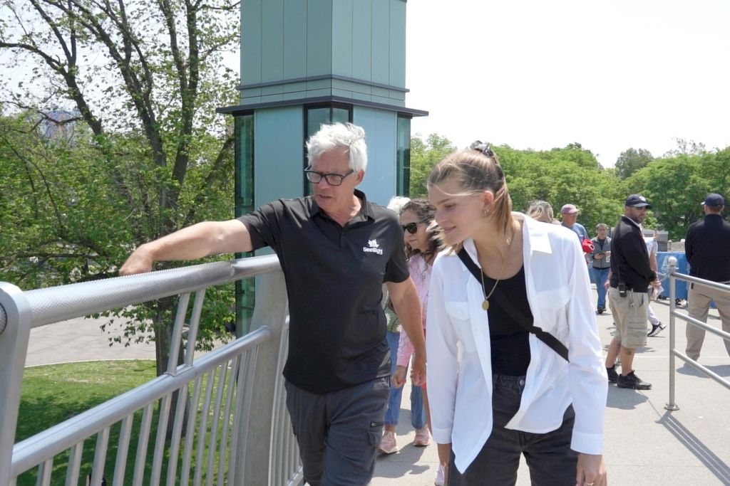 검은색 셔츠를 입은 남성과 흰색 셔츠를 입은 여성을 비롯해 다리를 걷고 있는 사람들로, 푸른 나무가 배경을 이루고 있습니다.