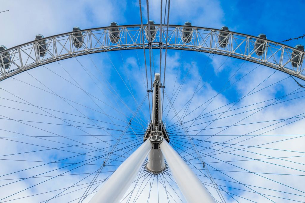 휠 스포크와 조수석 캡슐을 보여주는, 흐린 푸른 하늘을 배경으로 대관람차 구조물의 위쪽 모습.