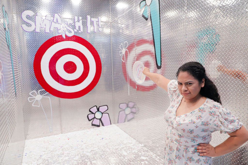 만화 같은 꽃과 롤리팝 그래픽이 돋보이는 금속 벽의 대상을 가리키는 꽃무늬 드레스를 입은 여성.